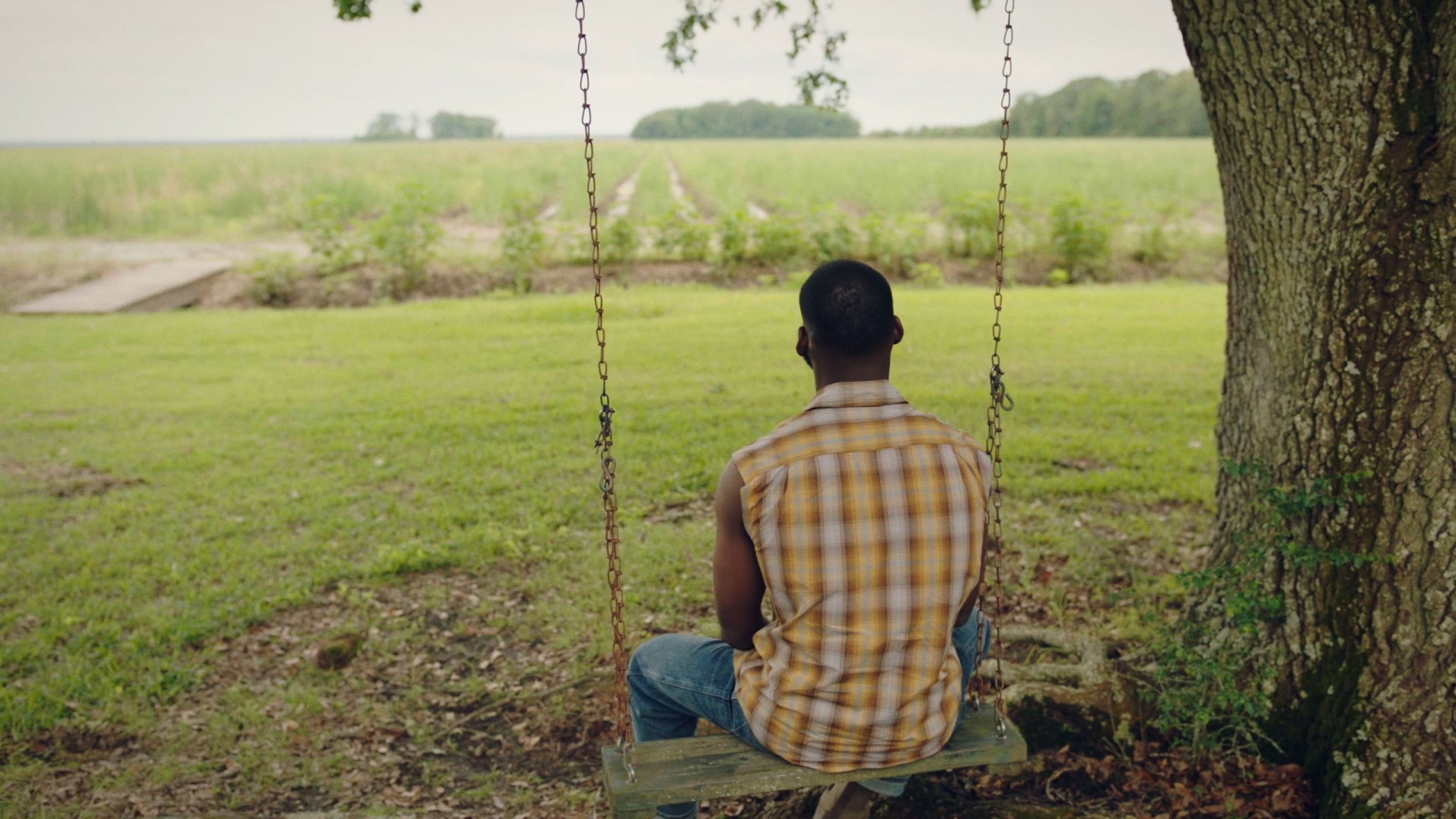 Kofi Siriboe as Ralph Angel Bordelon, sits on a swing.