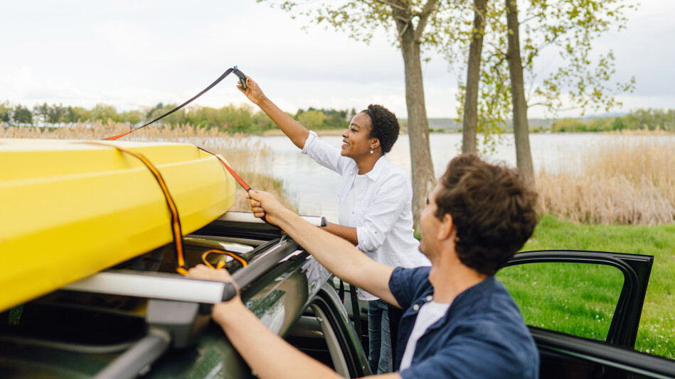 Mixed race couple securing kayak to the roof of their car