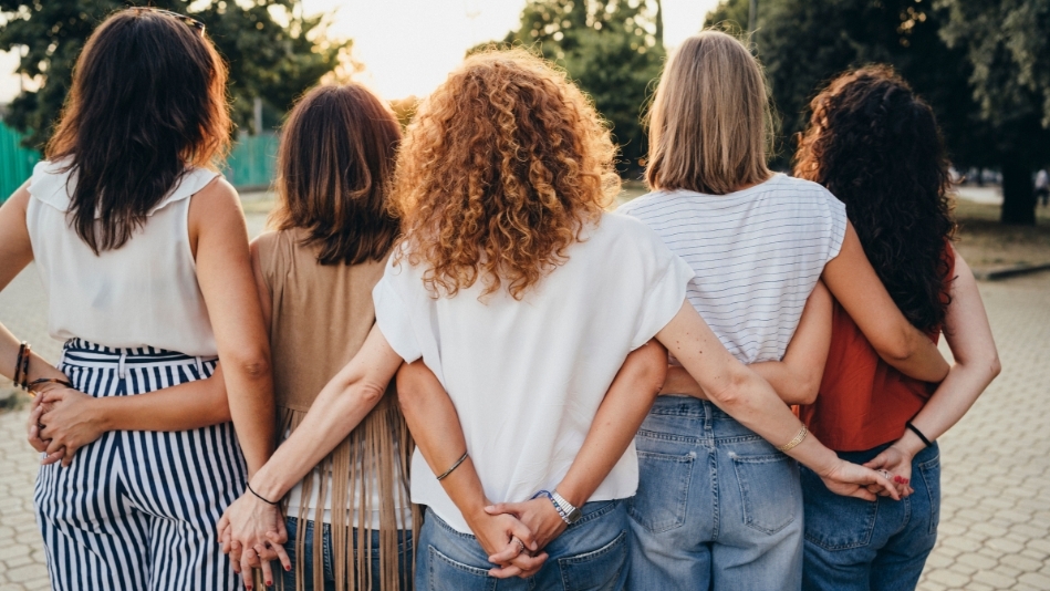 Group of women friends holding hands together against sunset